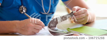 Male doctor reading patient's medical history and taking notes while working at office desk. Male doctor reading patient's medical history and taking notes while working at office desk. 106715288