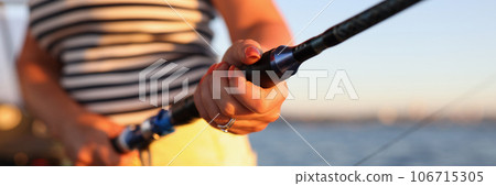 Woman is holding fishing rod while standing on boat, sea is in background. Woman is holding fishing rod while standing on boat, sea is in background. 106715305