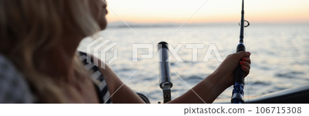 Fisherwoman holds spinning rod in her hands and looking at sea while fishing from boat. 106715308