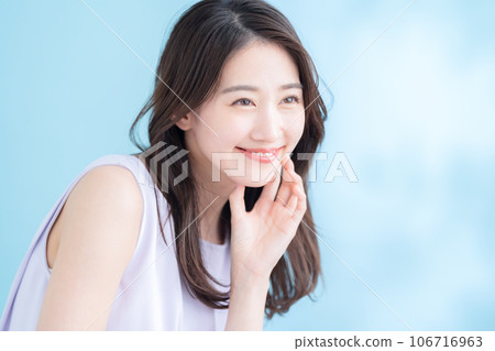 一位在陽光普照的藍色背景下做護膚的年輕女性 一位在陽光普照的藍色背景下做護膚的年輕女性 106716963