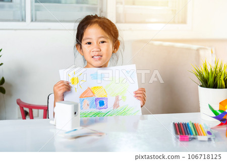 Happy child little girl lift up colorful drawing landscape my home dream on paper to camera, Asian cute kid preschooler smiling showing draw country house picture at home to learning arts homework 106718125