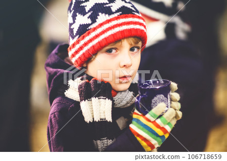 Little cute kid boy with cup of steaming hot chocolate or children punch. Happy child on Christmas market in Germany. Preschool kid in winter clothes warming hands on cup and drinking eggnog. Little cute kid boy with cup of steaming hot chocolate or children punch. Happy child on Christmas market in Germany. Preschool kid in winter clothes warming hands on cup and drinking eggnog. 106718659