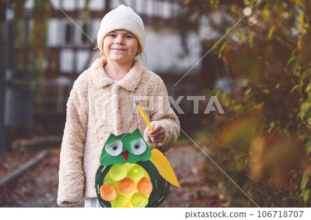 Little preschool kid girl holding selfmade traditional owl lanterns with candle for St. Martin procession. child happy about children and family parade in kindergarten. German tradition Martinsumzug Little preschool kid girl holding selfmade traditional owl lanterns with candle for St. Martin procession. child happy about children and family parade in kindergarten. German tradition Martinsumzug 106718707