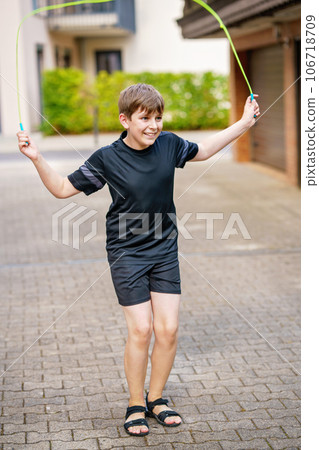 Handsome kid boy with skipping rope outdoors. Teenager boy jumping and training in sports camp. Handsome kid boy with skipping rope outdoors. Teenager boy jumping and training in sports camp. 106718709