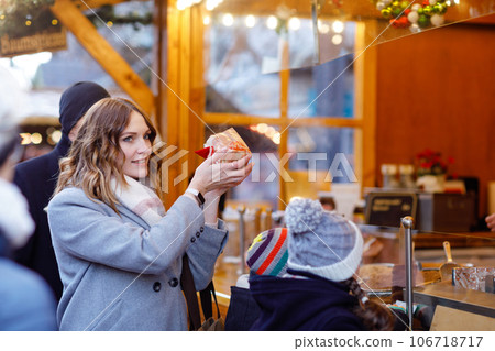 Beautiful young woman having fun on traditional Christmas market during strong snowfall. Happy girl buying traditional gingerbread called Lebkuchen. 106718717
