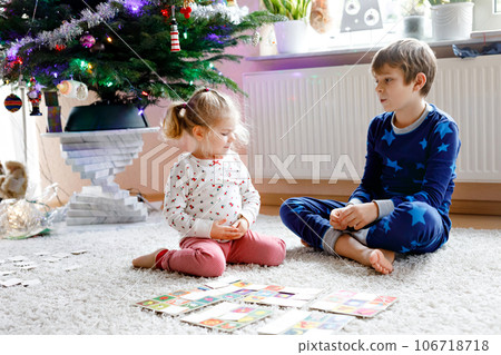 Two little chilren, cute toddler girl and school kid boy playing together card game by decorated Christmas tree. Happy healthy siblings, brother and sister having fun together. Family celebrating xmas Two little chilren, cute toddler girl and school kid boy playing together card game by decorated Christmas tree. Happy healthy siblings, brother and sister having fun together. Family celebrating xmas 106718718