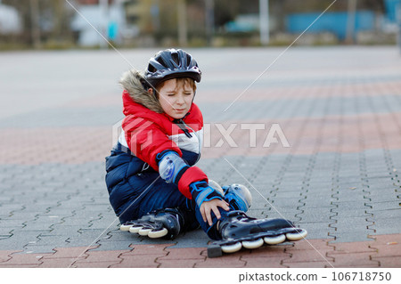 Little school kid boy skating with rollers in the city. child in protection safety clothes. Active schoolboy making sports and learning to skate on inline skater. Falling down and getting hurt 106718750