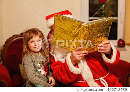 Little toddler girl talking to Santa Claus called Nikolaus or Weihnachtsmann in German. Happy smiling kid waiting for gifts. Santa with golden book. Xmas, childhood, holiday Little toddler girl talking to Santa Claus called Nikolaus or Weihnachtsmann in German. Happy smiling kid waiting for gifts. Santa with golden book. Xmas, childhood, holiday 106718789