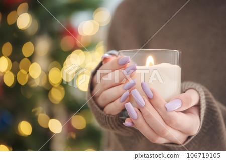The hands of a young girl with a beautiful light purple manicure hold a candle 106719105