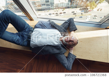 Top view of tired smiling senior businessman resting on wooden banch in office during break time Top view of tired smiling senior businessman resting on wooden banch in office during break time 106721368