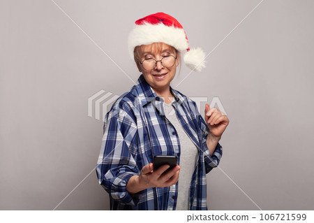 Senior woman granny in red Santa hat using smartphone, Christmas portrait Senior woman granny in red Santa hat using smartphone, Christmas portrait 106721599