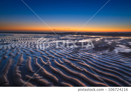 A seascape during sunset. Lines of sand on the seashore. Bright sky during sunset. A seascape during sunset. Lines of sand on the seashore. Bright sky during sunset. 106724216