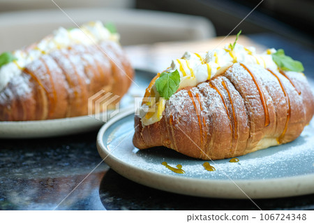 Sweet croissant sandwich dessert filled with whipped cream mixed with custard on blue plate Sweet croissant sandwich dessert filled with whipped cream mixed with custard on blue plate 106724348