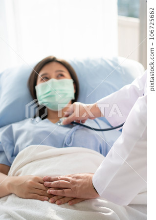 Women Asian doctors hold the patient hand and encourage and provide medical advice While doctors use Stethoscope for checking the patient heart in bed. Concept of Care and compassion Women Asian doctors hold the patient hand and encourage and provide medical advice While doctors use Stethoscope for checking the patient heart in bed. Concept of Care and compassion 106725662