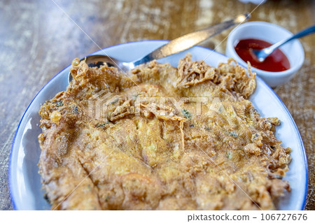 Close-up shallow field of view of Thai style omelet by mixing eggs with coriander and stirring well Fry in hot oil until the egg is cooked, yellow, fragrant, with a small cup of tomato sauce. 106727676