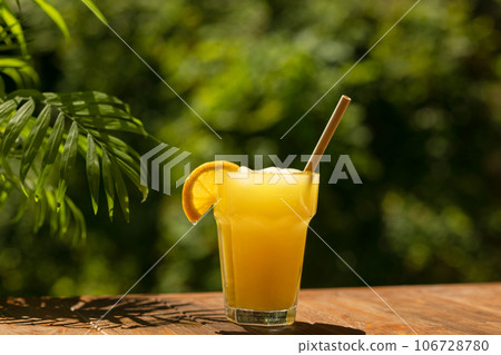 glass of tasty orange juice standing on an outdoor wooden table 106728780