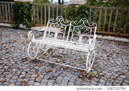 Iron white vintage rocking bench on paving stones in the courtyard of the house 106728790