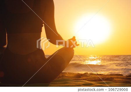 Close-up woman's hand practicing yoga silhouette, meditation in lotus position on the beach, feel so comfortable and relax on vacation with golden light, healthy concept 106729008