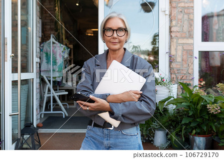 a gray-haired mature dreamy woman dressed for summer stopped on the street near the porch of a cafe 106729170