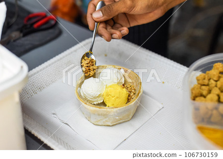 Hand holding coconut and mango ice cream in coconut shell in Jalan Alor street food market in Kuala Lumpur Hand holding coconut and mango ice cream in coconut shell in Jalan Alor street food market in Kuala Lumpur 106730159