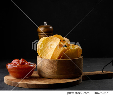 Potato chips in a wooden bowl and a bowl of sauce on a black table, snack Potato chips in a wooden bowl and a bowl of sauce on a black table, snack 106730630