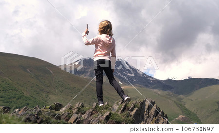 Little girl taking photos of mountains while standing on the edge of cliff Little girl taking photos of mountains while standing on the edge of cliff 106730697