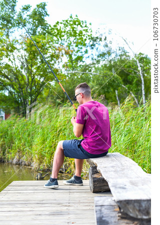 Young fisherman sitting on wooden pier, fishing in the lake. he holding the rod and looking at float 106730703