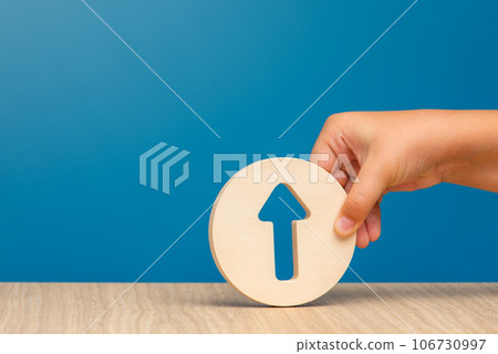 Arrow pointing up on a blue background. Banner with an arrow in a wooden circle in a hand close-up pointing up with copy space. Arrow pointing up on a blue background. Banner with an arrow in a wooden circle in a hand close-up pointing up with copy space. 106730997