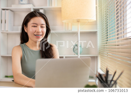 Woman using laptop to work or do homework at home with smiling face in her office, Creating happiness at work with a smile, Live performance or vdo call with laptop, Work from home. 106731013