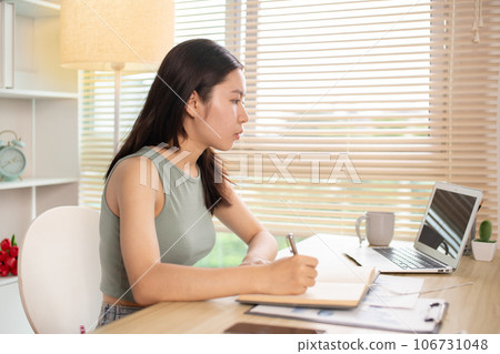 Beautiful young asian woman watching live video or video call of teacher teaching on laptop in her home, Take notes of important conversations and messages during the teacher's teaching. Beautiful young asian woman watching live video or video call of teacher teaching on laptop in her home, Take notes of important conversations and messages during the teacher's teaching. 106731048