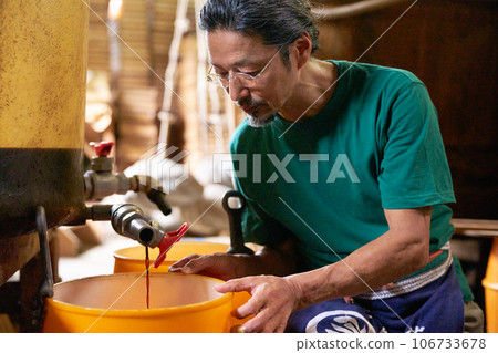 A craftsman checks the squeezed soy sauce at a soy sauce manufacturing factory. A craftsman checks the squeezed soy sauce at a soy sauce manufacturing factory. 106733678