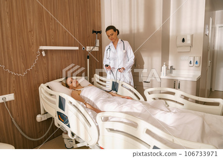 Doctor checking blood pressure of sick woman patient in ward of modern clinic 106733971