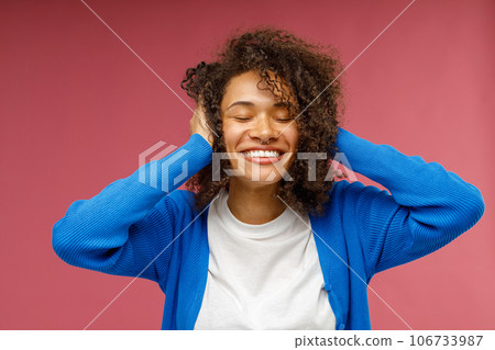 Pretty woman with closed eyes touching curly hair standing on red studio background Pretty woman with closed eyes touching curly hair standing on red studio background 106733987