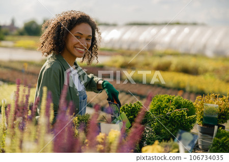 Professional woman garden worker takes care of plants in botanic shop on greenhouse background Professional woman garden worker takes care of plants in botanic shop on greenhouse background 106734035