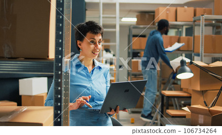 Warehouse owner checking cardboard boxes from storage space shelves, using laptop to plan stock inventory and take notes. Entrepreneur working on startup development and supply chain. Warehouse owner checking cardboard boxes from storage space shelves, using laptop to plan stock inventory and take notes. Entrepreneur working on startup development and supply chain. 106734264