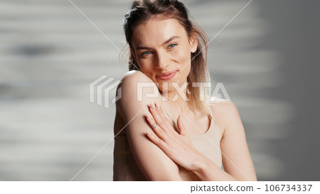 Caucasian lady promoting body cream in studio, filming beauty ad campaign and applying moisturizer and neck and shoulders. Beautiful model using glowing serum and advertising product. Caucasian lady promoting body cream in studio, filming beauty ad campaign and applying moisturizer and neck and shoulders. Beautiful model using glowing serum and advertising product. 106734337