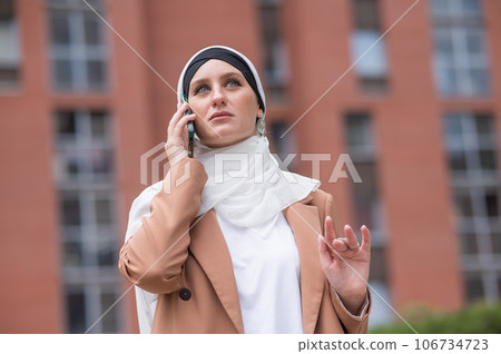Young woman in hijab talking on smartphone outdoors. Young woman in hijab talking on smartphone outdoors. 106734723