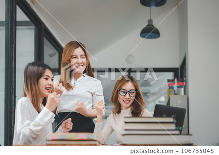 Three businesswomen show joyful expression of success at work smiling happily with a laptop computer in a modern office. 106735048