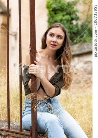 Woman in unbuttoned blouse posing near fence Woman in unbuttoned blouse posing near fence 106735955