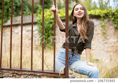 Woman posing near fence against abandoned building Woman posing near fence against abandoned building 106735985
