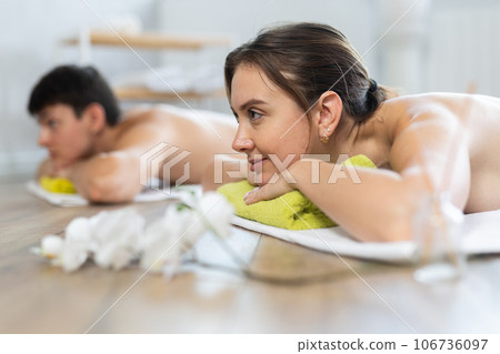 After massage, girl lies on white blanket on floor. Blurry unrecognizable clients guy in background After massage, girl lies on white blanket on floor. Blurry unrecognizable clients guy in background 106736097