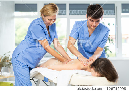 Young masseur providing massage to woman under supervision of female mentor 106736098
