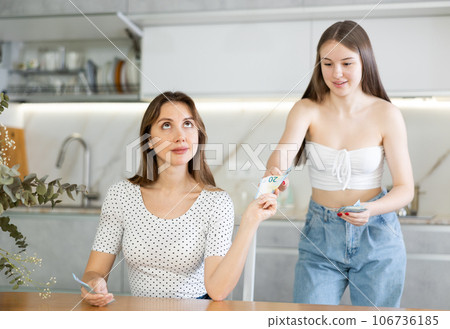 Young woman giving money to her sister in kitchen 106736185