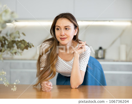 Smiling middle-aged woman posing leaning on kitchen table 106736204