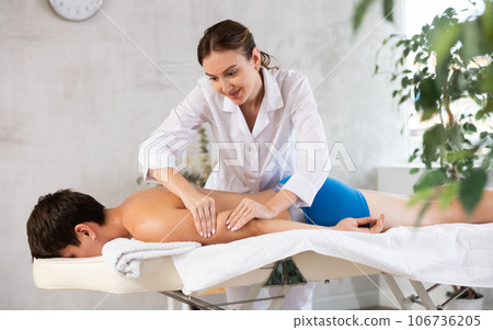 Guy lies face down on couch and enjoys massage session, physiotherapist girl works out clients hand 106736205