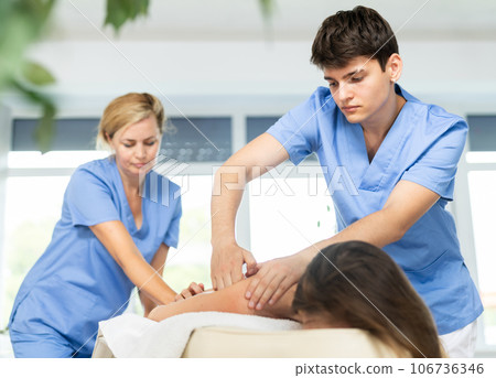 Two unrecognizable female and male masseuses perform stroking and rubbing of muscle of back to girl Two unrecognizable female and male masseuses perform stroking and rubbing of muscle of back to girl 106736346