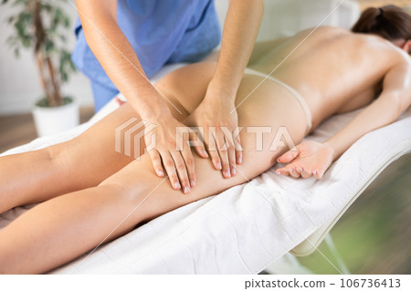 Hands of masseur performing leg massage for young female patient Hands of masseur performing leg massage for young female patient 106736413