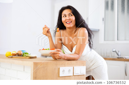 Portrait of positive woman in nightdress eating salad at home 106736532