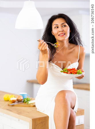 Portrait of positive woman in nightdress eating salad at home Portrait of positive woman in nightdress eating salad at home 106736540