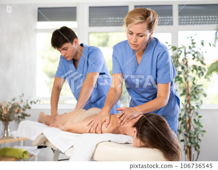 Skilled masseuse performing massage to woman in tandem with assistant 106736545
